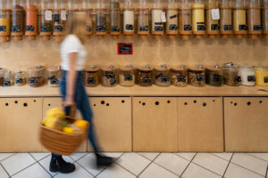 A young customer walks past a shelf with filling containers for grain, detail from an unwrapped shop. A young customer walks past a shelf with filling containers for grain, detail from an unwrapped shop.